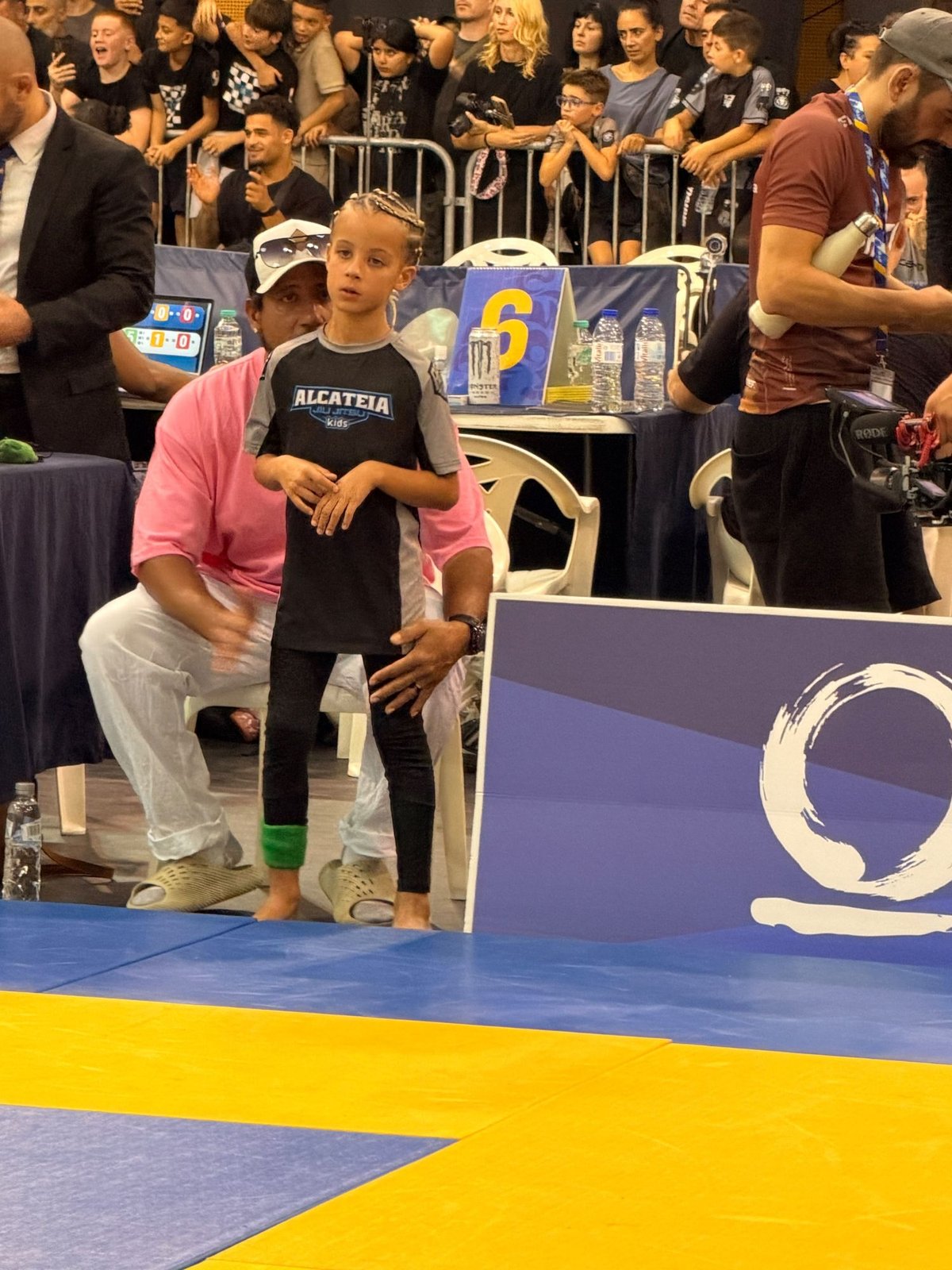 Aleyna at the edge of the mat with her father in her corner, moments before her match at the European Kids No-Gi IBJJF Championship, Lisbon 2026.