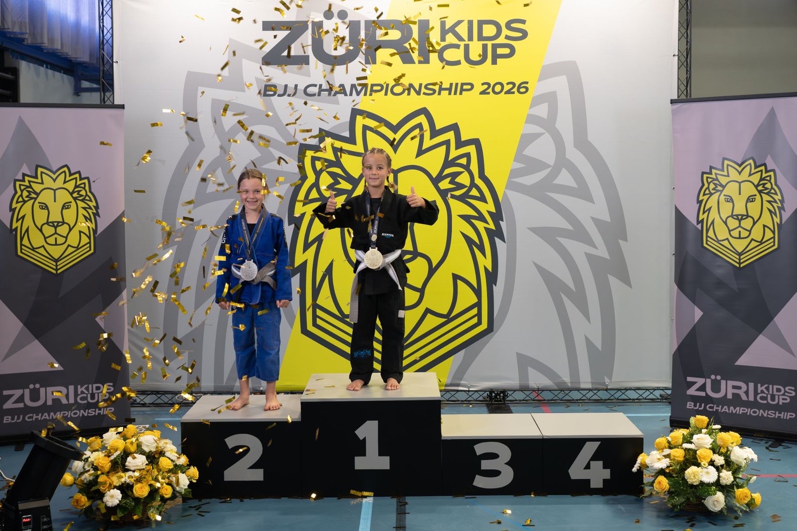 Aleyna on the top step of the podium with the Gi gold medal at the Züri Kids Cup BJJ Championship 2026, confetti falling.